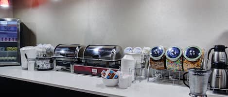 Een ontbijtbuffet met koffieautomaten, melkdispensers en bakken met ontbijstgranen.