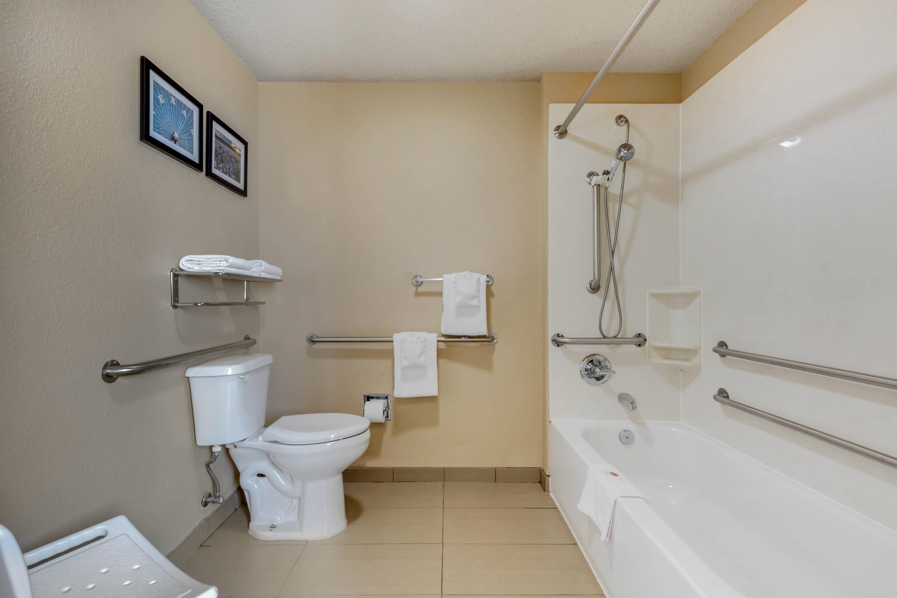 A bathroom with a toilet, a bathtub, and a shower. There are handrails and a towel rack.