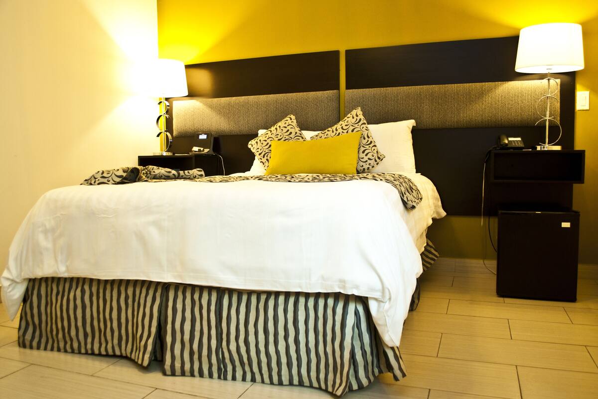 A neatly made bed with a white and black striped skirt, two bedside tables with lamps, and a black nightstand with a phone.