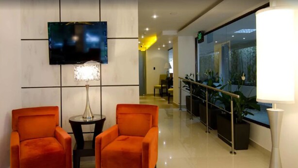 Un hall d’entrée avec deux fauteuils orange, un téléviseur fixé au mur, une lampe et une vue sur un balcon agrémenté de plantes.