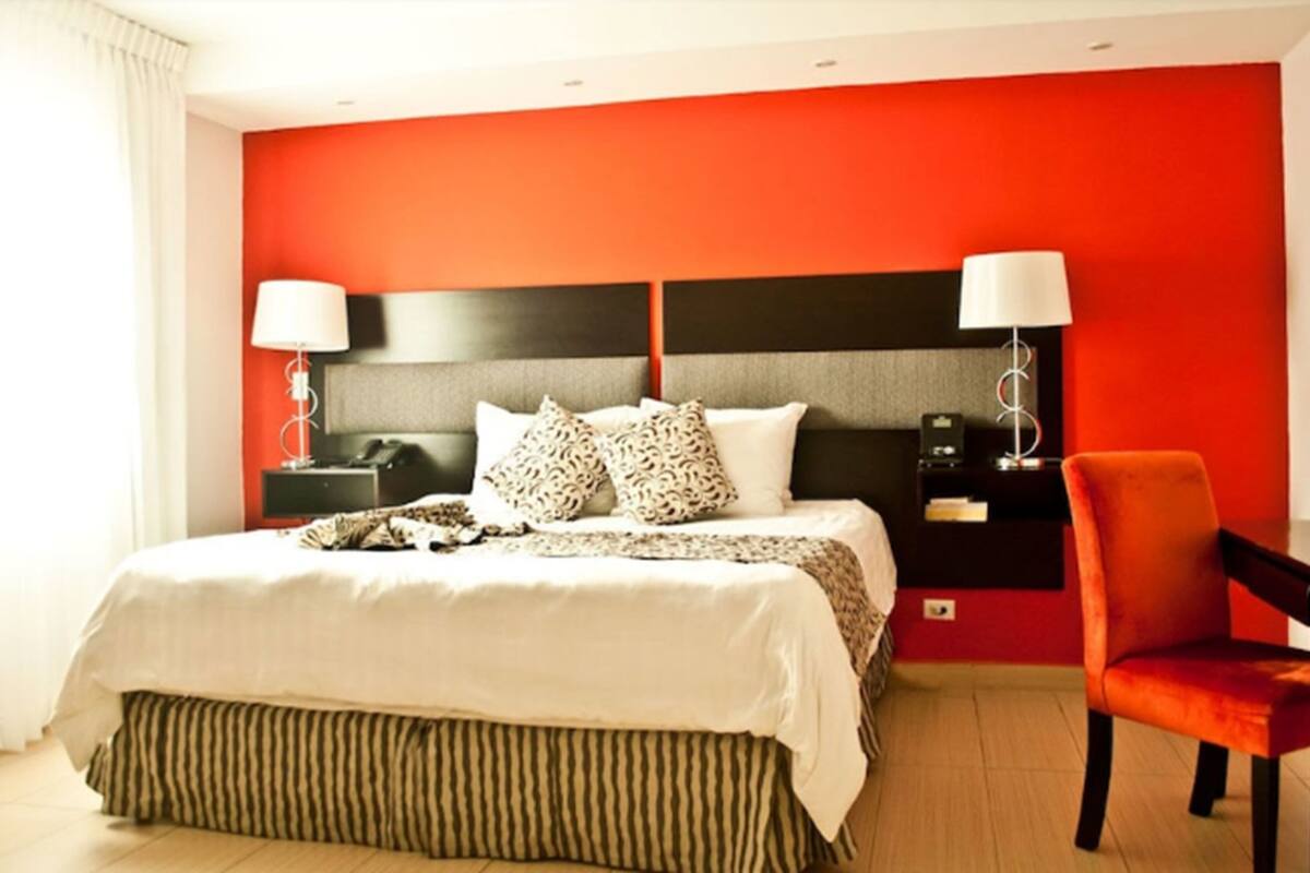 A hotel room with a large bed, two bedside tables, a chair, and a desk with a lamp.