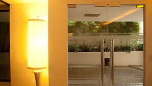 L’entrée d’un hôtel, avec une porte en verre, une lampe et une vue sur un jardin planté.