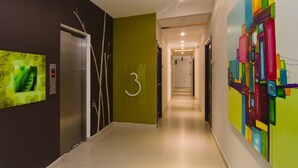 Un couloir moderne doté d’un ascenseur numérique, d’une plaque portant le chiffre « 3 » et d’œuvres d’art murales abstraites et colorées.