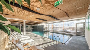 Un área de piscina interior moderna con techo de madera, paredes de vidrio y sillones de descanso.