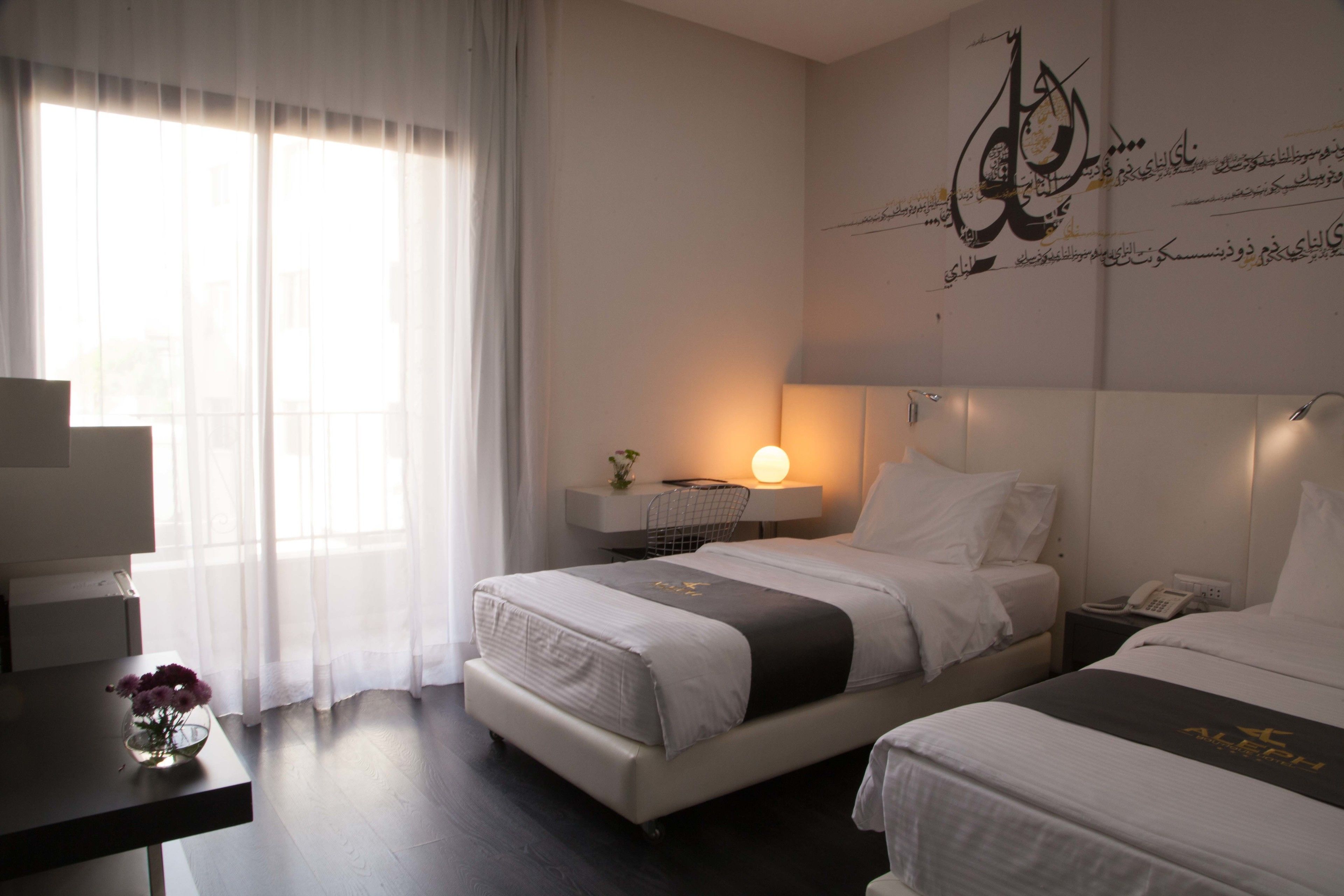 Ein Hotelzimmer mit zwei Betten, einem Schreibtisch, einer Lampe und einer Wand mit arabischer Kalligraphie.