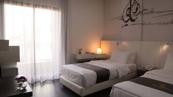 Ein Hotelzimmer mit zwei Betten, einem Schreibtisch, einer Lampe und einer Wand mit arabischer Kalligraphie.