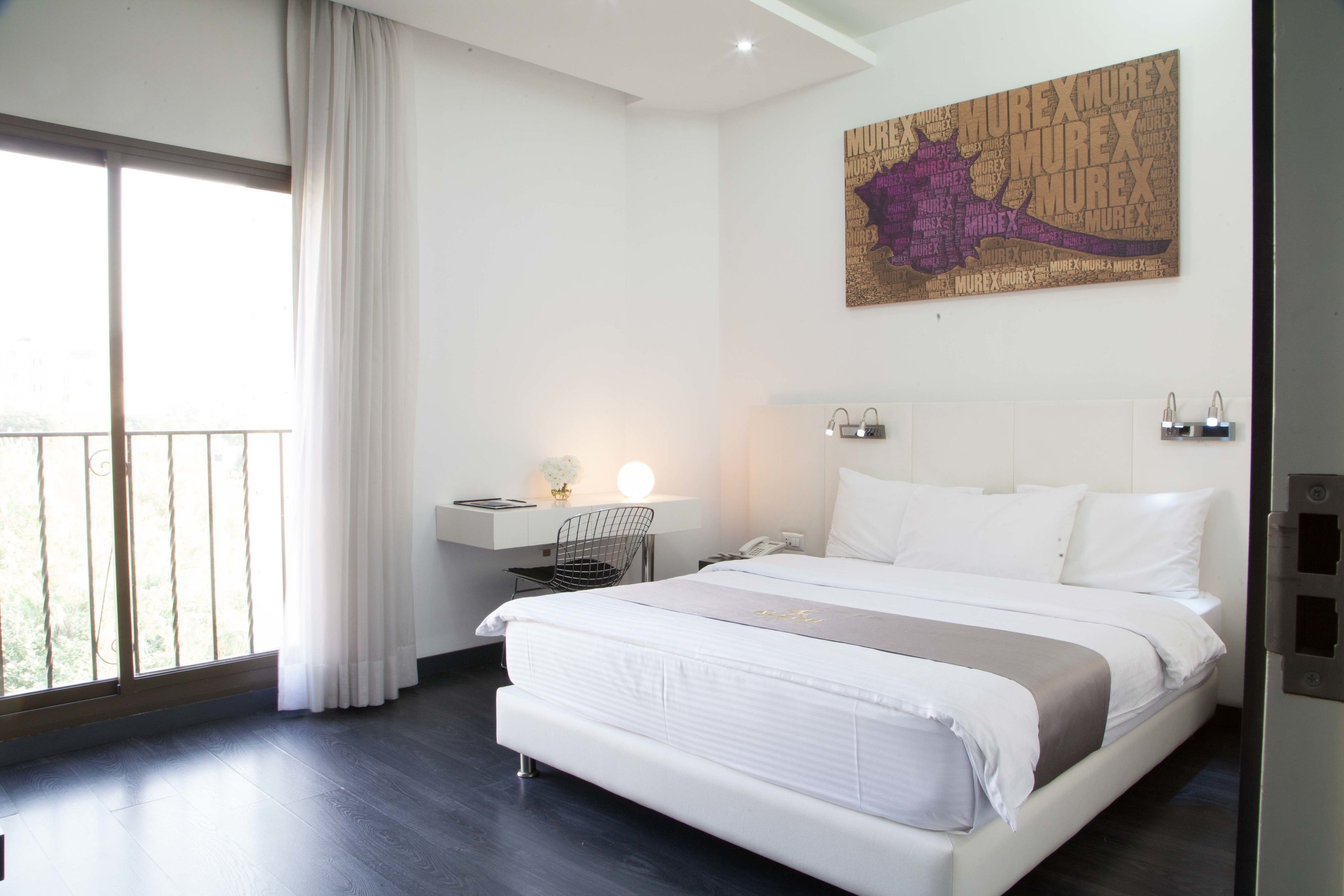 Una habitación de hotel moderna con una cama grande, un escritorio con lámpara y una ventana con cortinas.