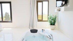 A modern bathroom with a large bathtub, a digital control panel, and a potted plant.