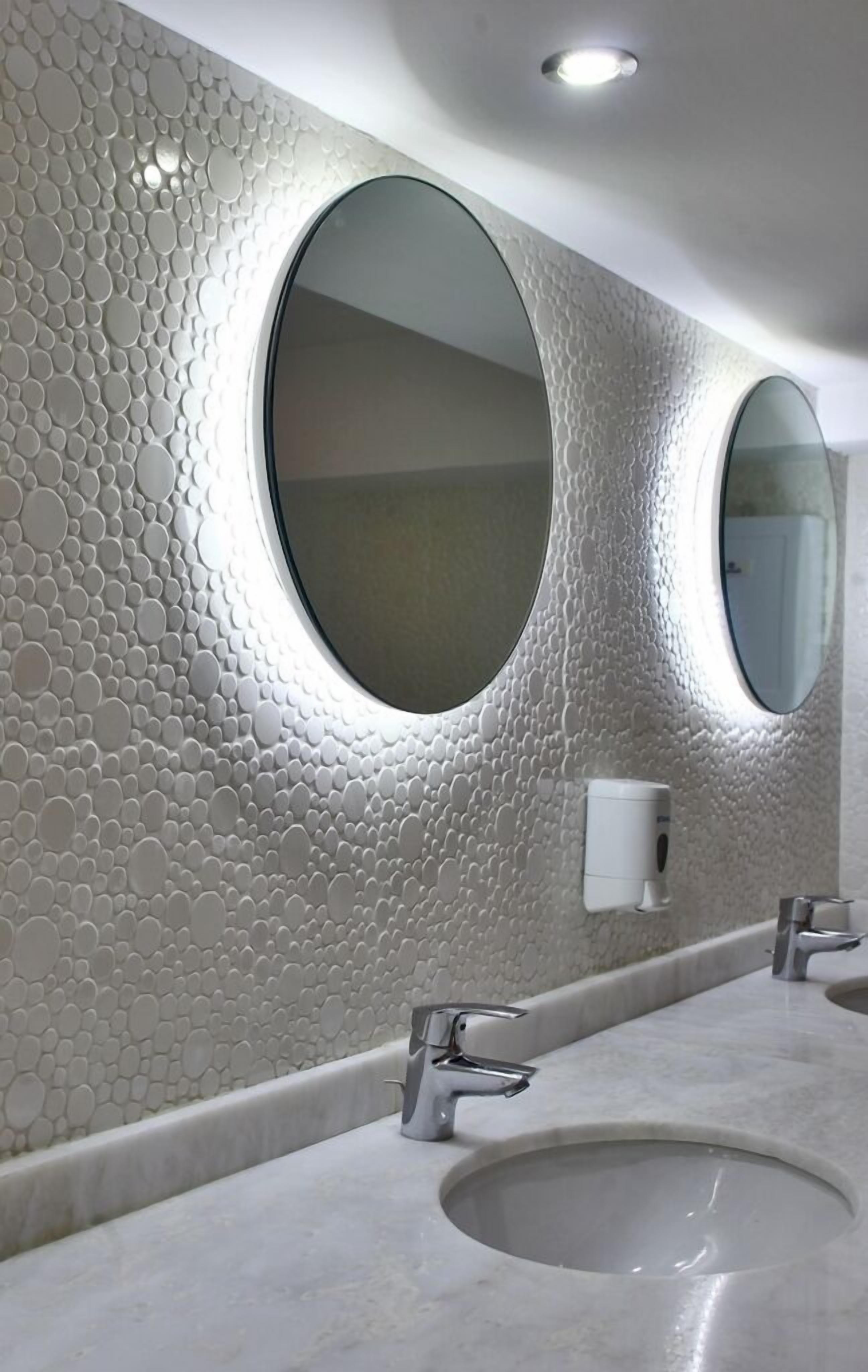Un baño con pared texturizada, dos espejos redondos, un lavabo y un grifo.