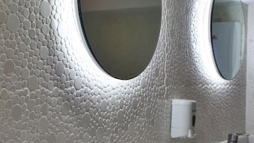 Un baño con pared texturizada, dos espejos redondos, un lavabo y un grifo.