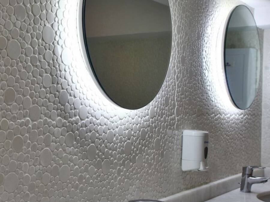 Un baño con pared texturizada, dos espejos redondos, un lavabo y un grifo.