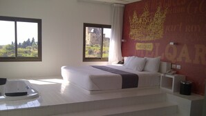 A modern hotel room with a large bed, a bathtub, and a view of the outdoors through the windows.