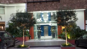 A modern building entrance with glass doors, potted plants, and a wooden deck.