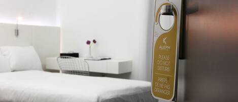 A hotel room with a bed, a desk, and a wall-mounted sign with a key symbol and text in multiple languages.