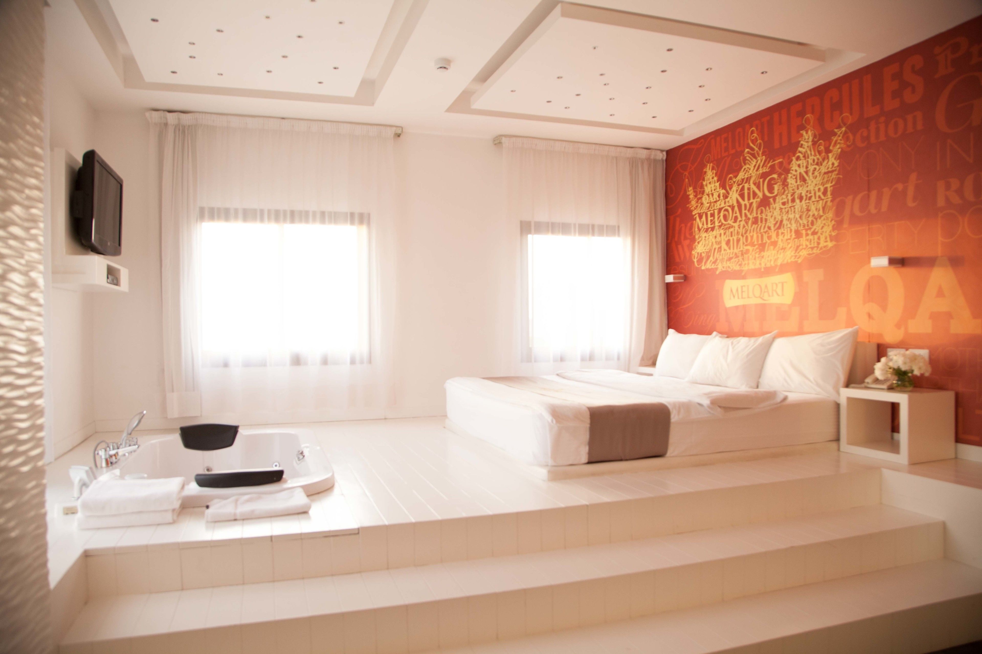 A modern bedroom with a large bed, a built-in bathtub, and a mural on the wall.
