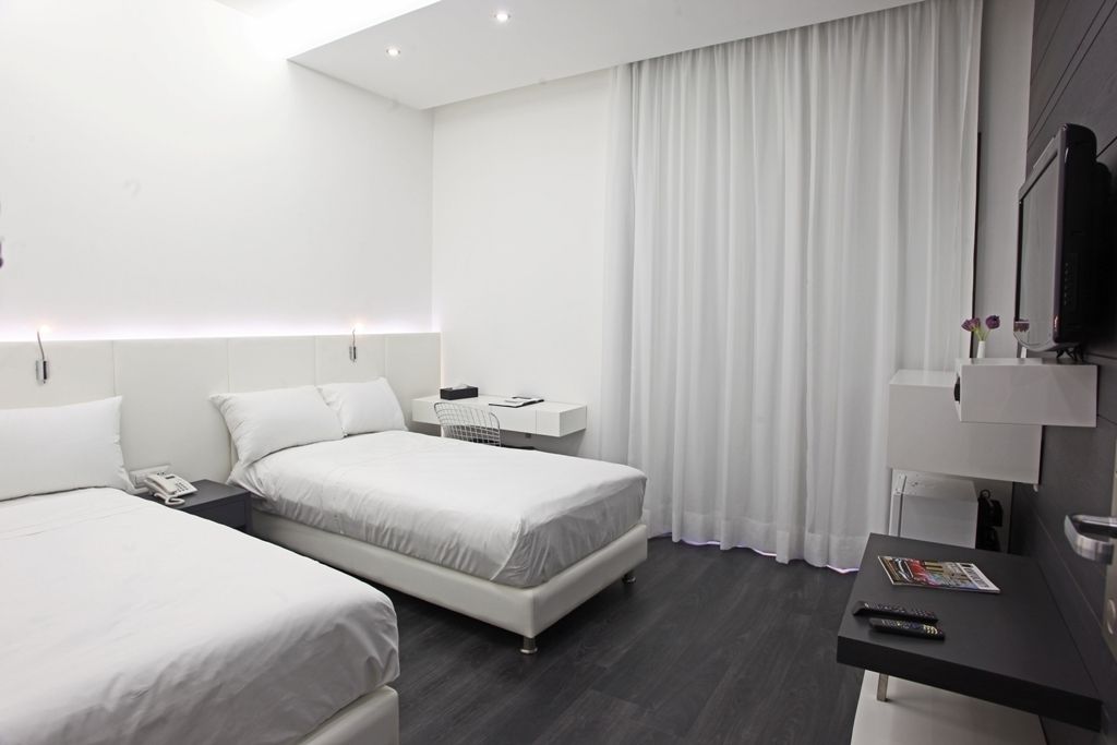 A modern hotel room with two beds, a desk, a TV, and a window with curtains.