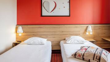 A hotel room with two beds, a red wall, and a framed artwork above the beds.