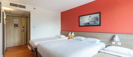 Habitación de hotel con dos camas, una pared de acento roja y un cuadro enmarcado sobre las camas.