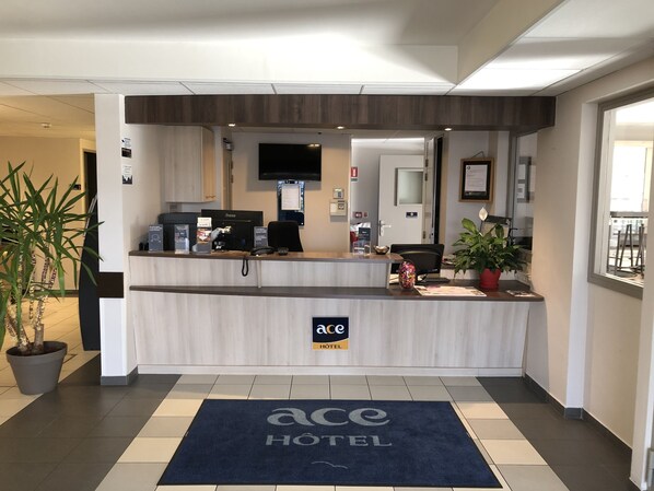 Un mostrador de recepción de hotel con un televisor de pantalla plana, una cafetera y una planta en maceta.