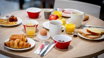 Una mesa de desayuno con cruasanes, tostadas, huevos, jugo de naranja y café.