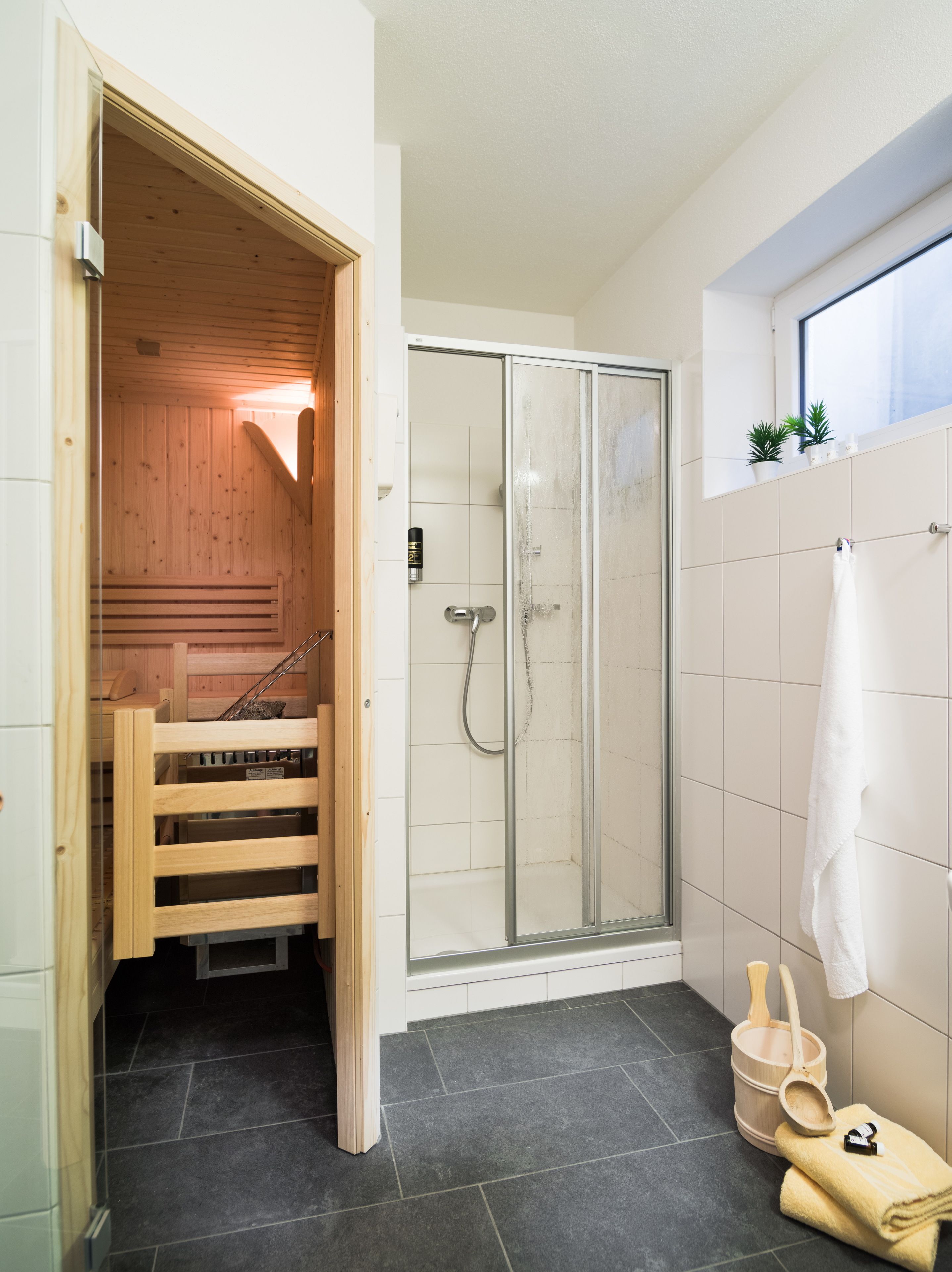 A modern bathroom with a glass shower enclosure, a wooden bench, and a towel rack.
