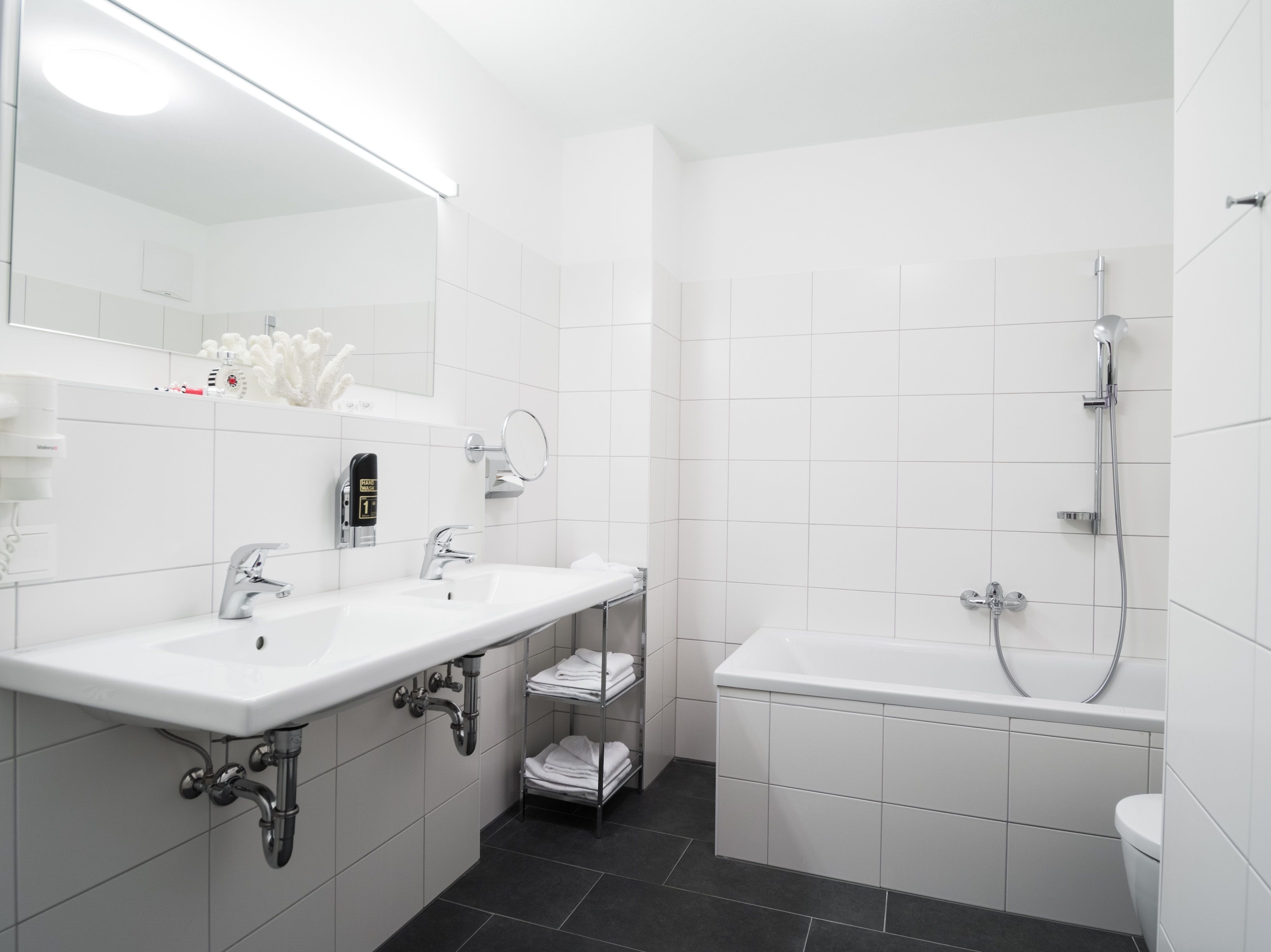 A modern bathroom with two sinks, a mirror, a shower, and a toilet.