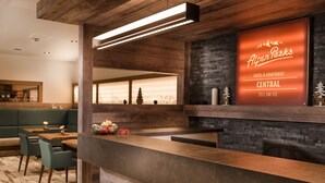 Een hotel receptie met een houten receptiebalie, een zithoek met groen gestoffeerde banken en een groot verlicht bord voor Alpen Parks Central.