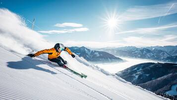 Ein Skifahrer mit gelber Jacke auf einem verschneiten Hang, im Hintergrund Berge.