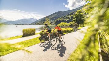 Två cyklister på en asfalterad stig vid en sjö, med berg i bakgrunden.