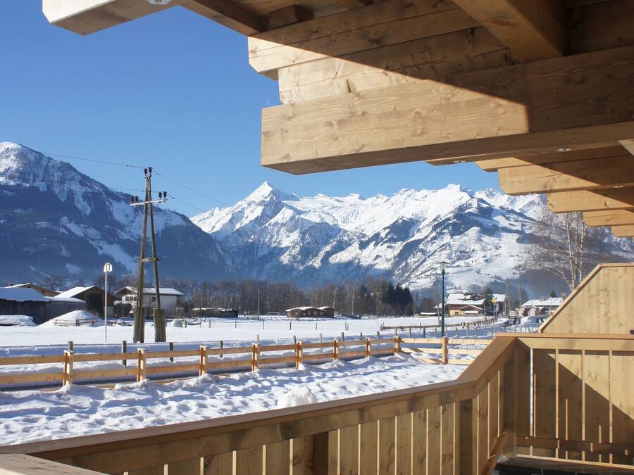 A wooden deck with a view of snow-covered mountains and a clear sky.