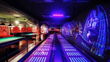 A pool hall with multiple tables and a neon-lit mural on the wall.
