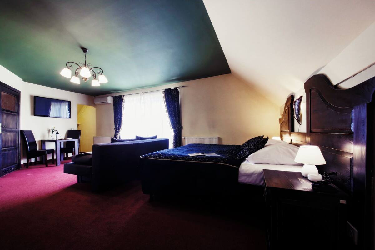 A hotel room with a bed, bedside table, lamp, and a desk with chairs.