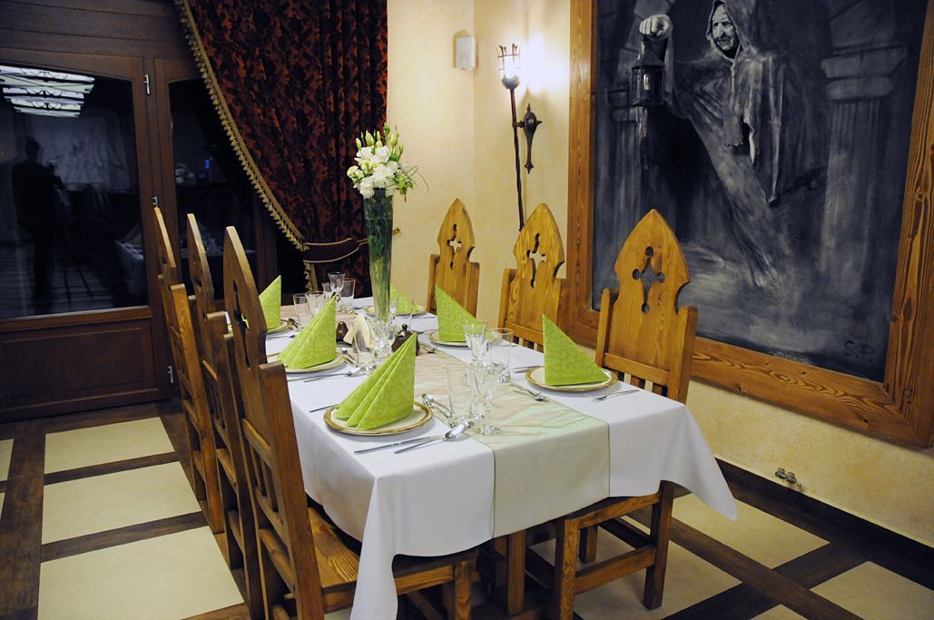 A dining table set with green napkins, plates, and cutlery, with a vase of flowers and a painting on the wall.