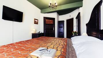 Habitación de hotel con una cama grande, un televisor de pantalla plana en la pared, una araña y una puerta que da a otra habitación.