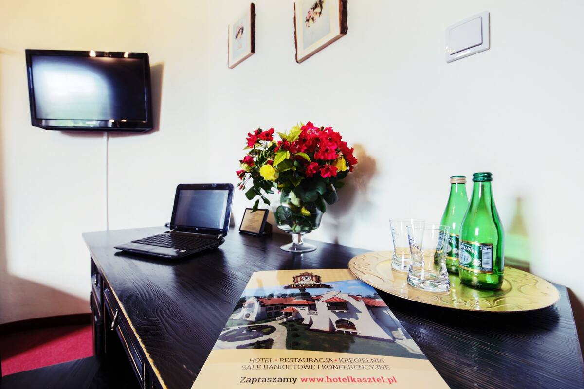 A hotel reception desk with a laptop, a vase of flowers, and a tray with glasses and green bottles.
