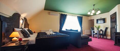 Una camera d'albergo con un letto, una scrivania con una lampada, una sedia, un tavolo con un vaso e un televisore appeso al muro.