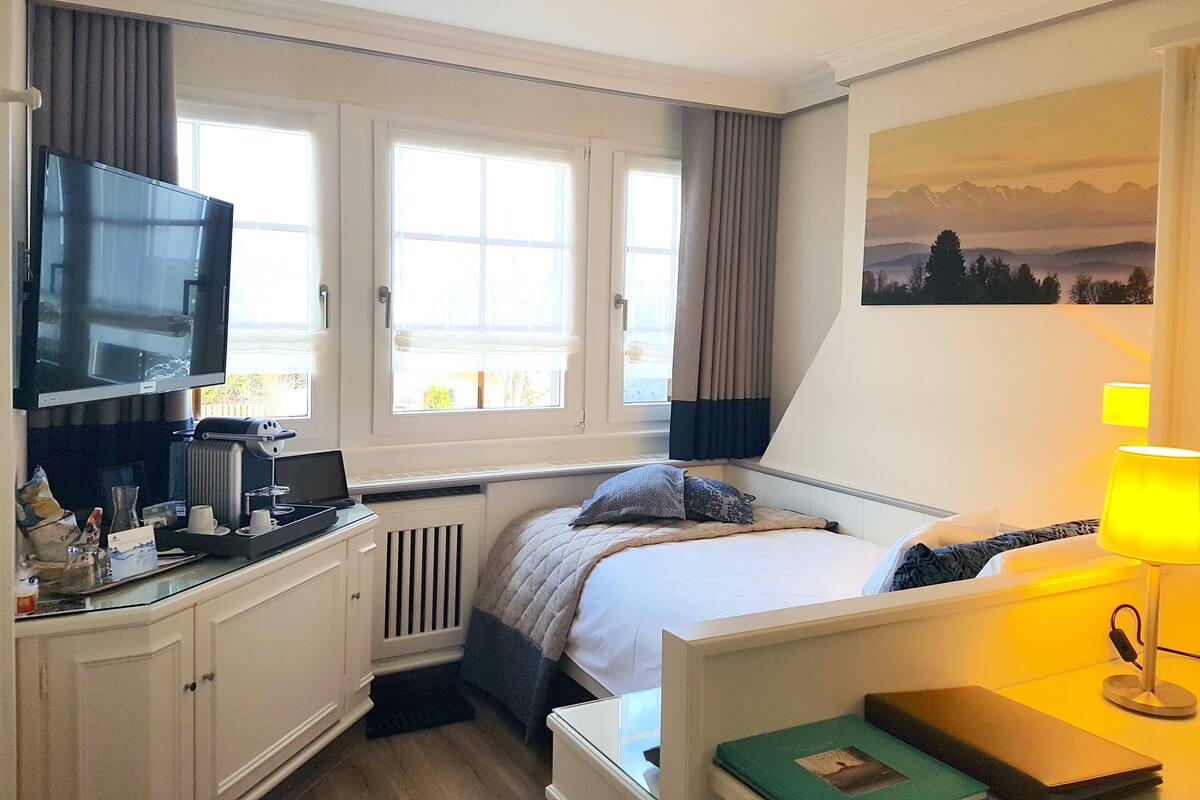 A hotel room with a bed, a TV, a desk, and a window with curtains.