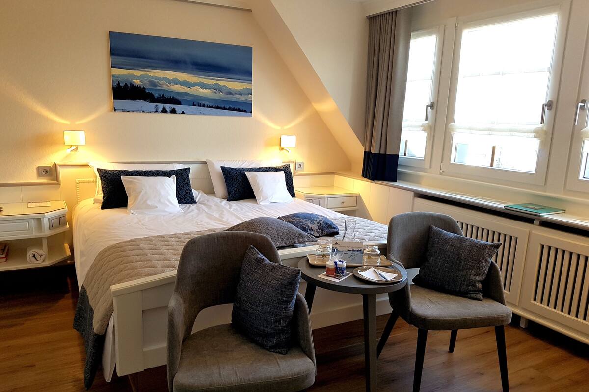 A hotel room with a large bed, two bedside tables, a desk, two armchairs, and a window with curtains.