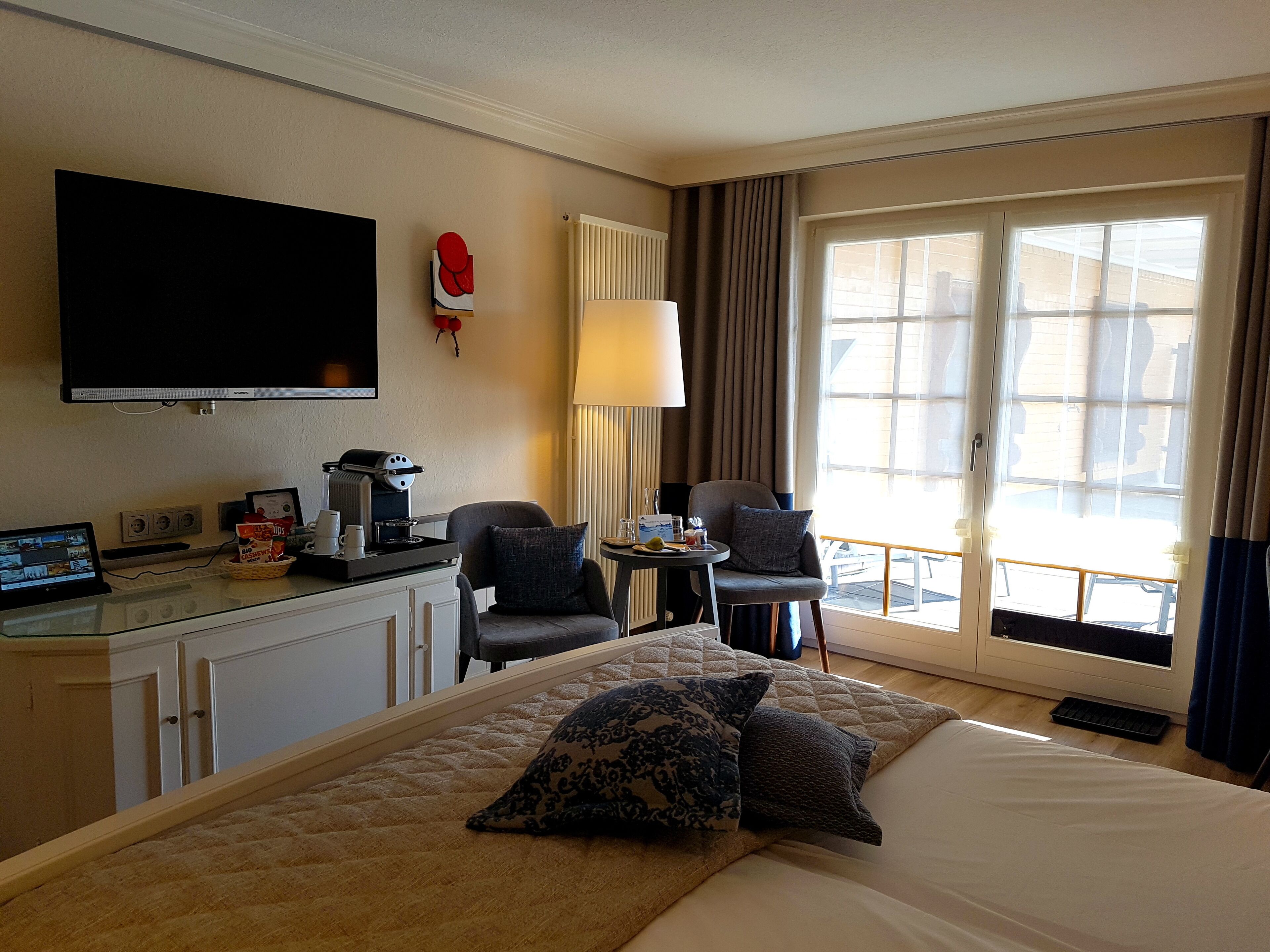 Una habitación de hotel con cama, escritorio con computadora, cafetera y televisión.