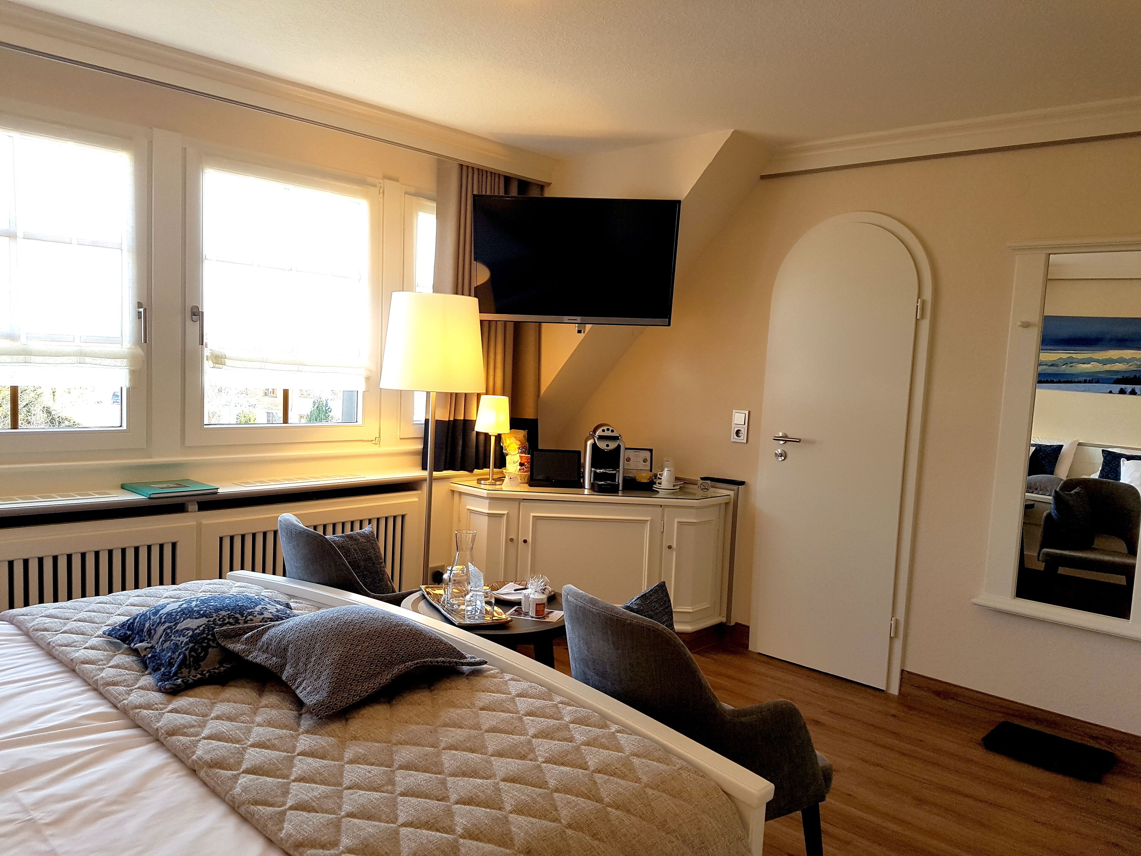 A hotel room with a bed, a desk with a lamp, a television, and a painting on the wall.