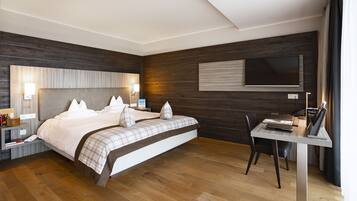 Een moderne hotelkamer met een groot bed, nachtkastjes, een bureau met stoel, een flatscreen-tv en houten lambrisering.