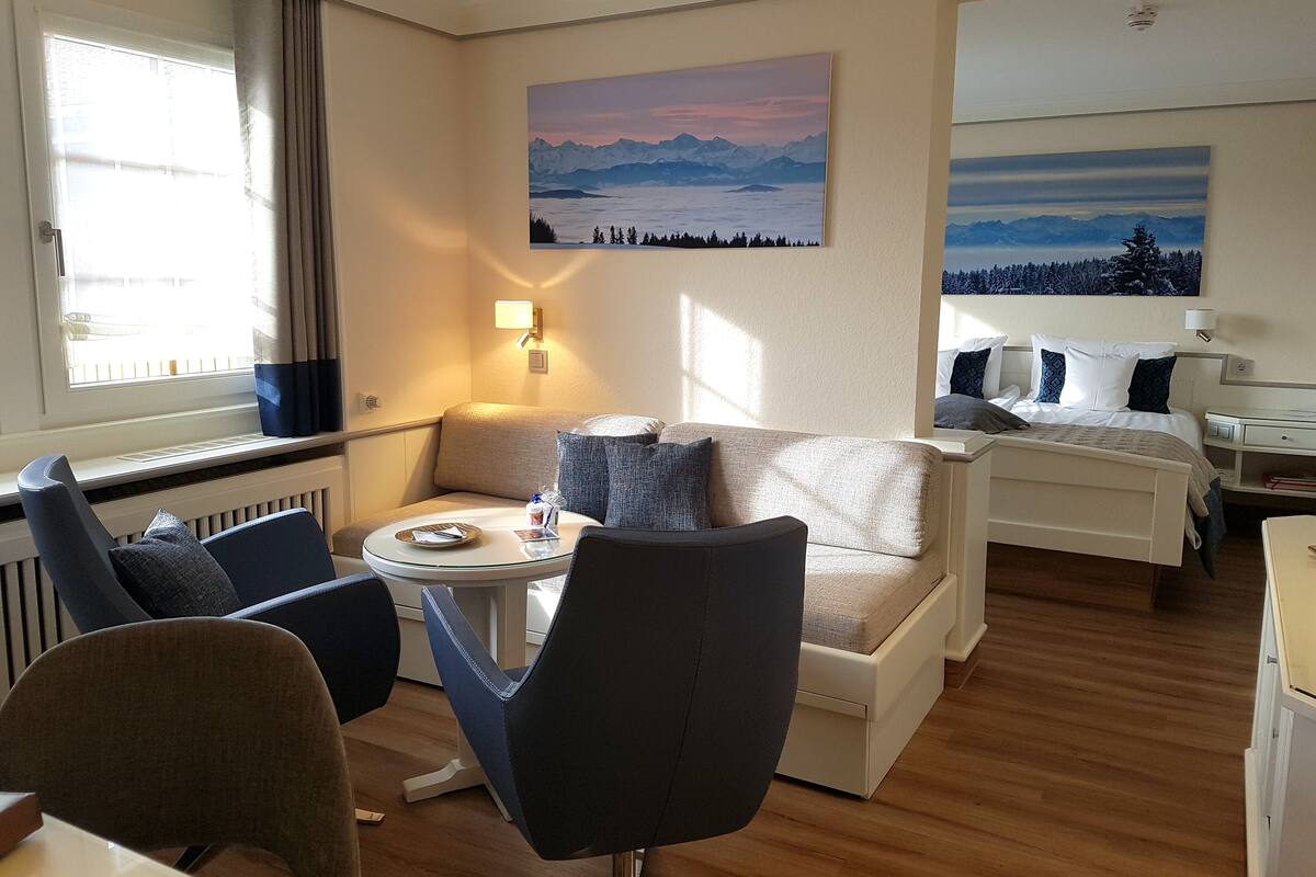 A modern hotel room with a sofa, two armchairs, a small round table, and a bed.