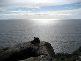 Una costa rocosa con una bota sobre una roca, con vista a un mar tranquilo bajo un cielo parcialmente nublado.