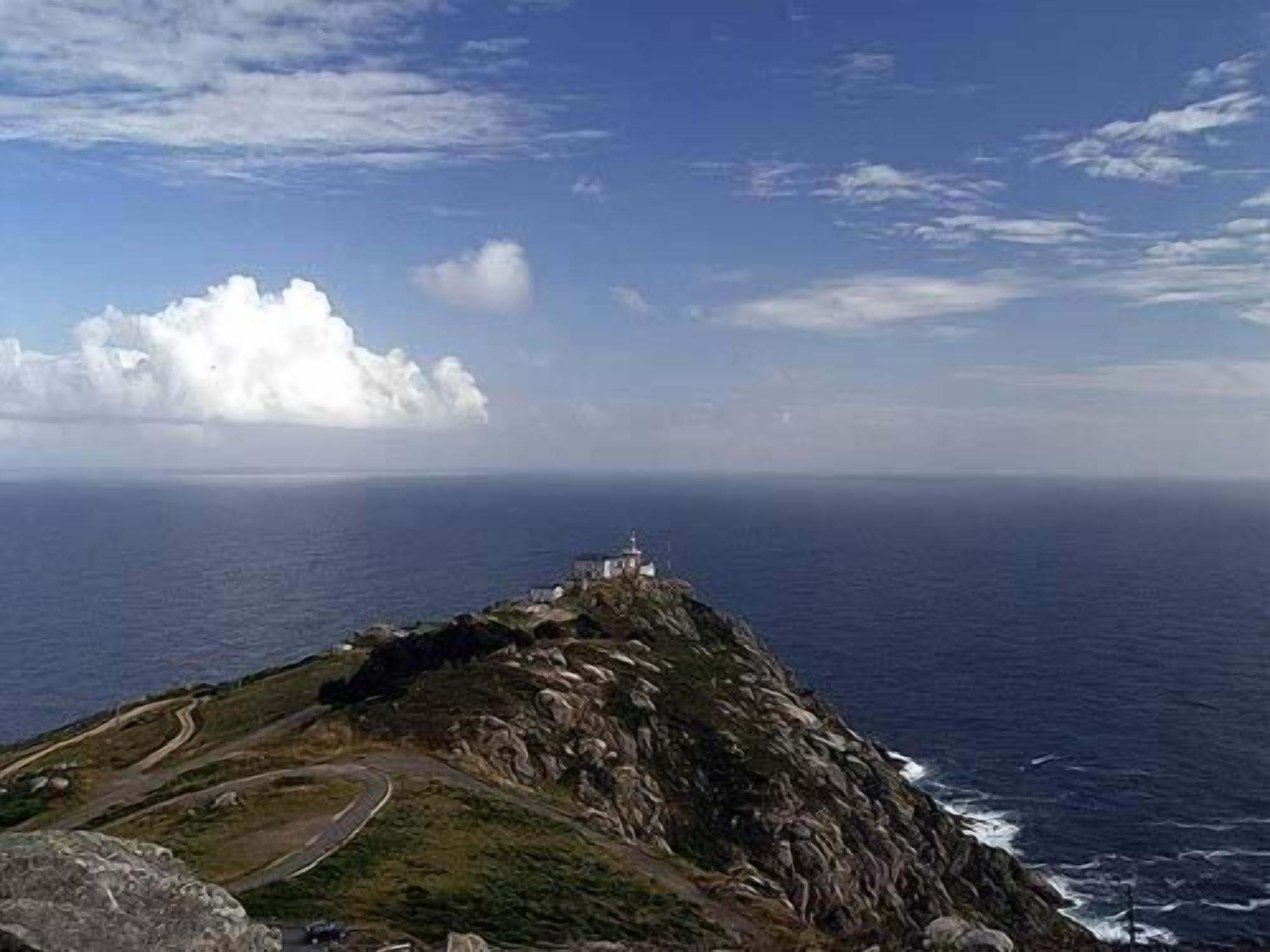 A coastal landscape with a winding road leading to a lighthouse on a rocky outcrop.