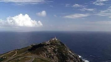 A coastal landscape with a winding road leading to a lighthouse on a rocky outcrop.