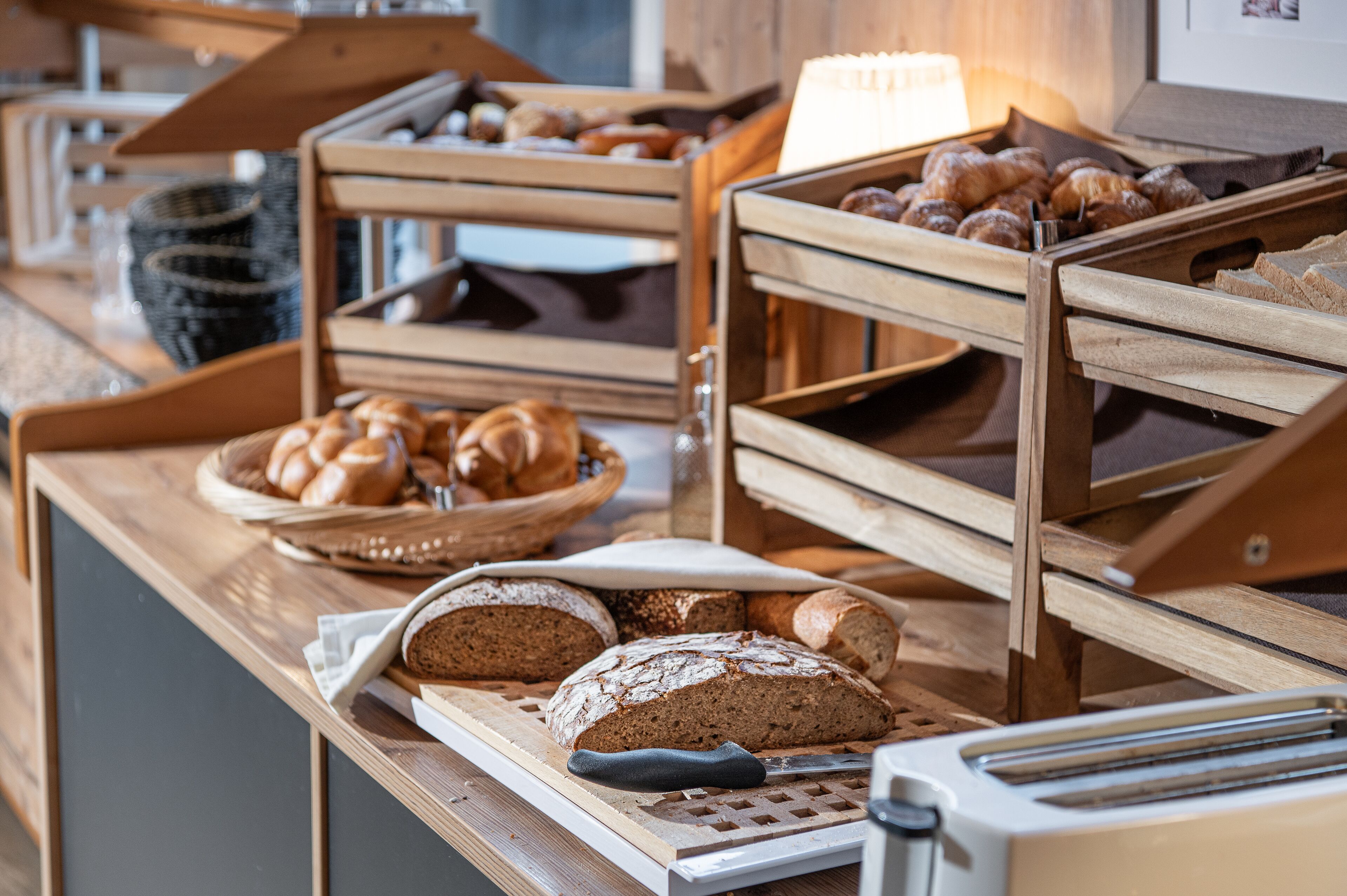 A buffet counter with various breads and pastries displayed in wooden trays.