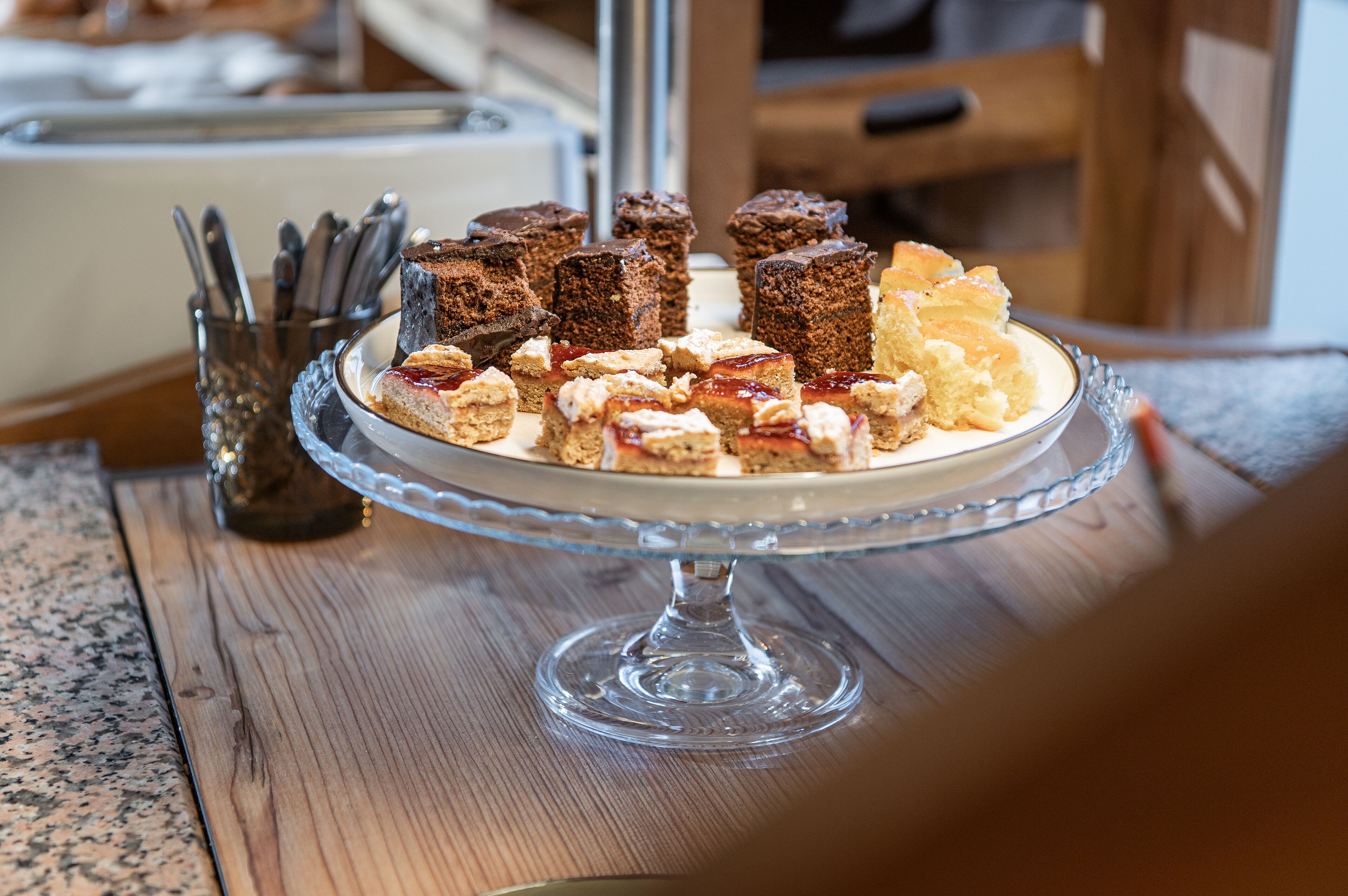 A glass cake stand with various desserts on a wooden table.
