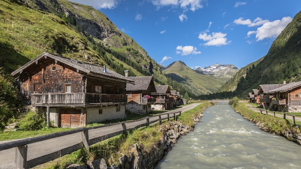 A row of wooden houses with balconies along a river, surrounded by mountains. - AlpenParks Hotel Montana Matrei (Matrei in Osttirol)
