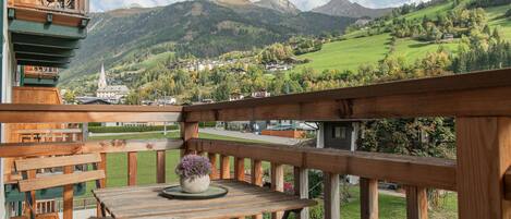 A wooden deck with a table and chairs, overlooking a village and mountains.