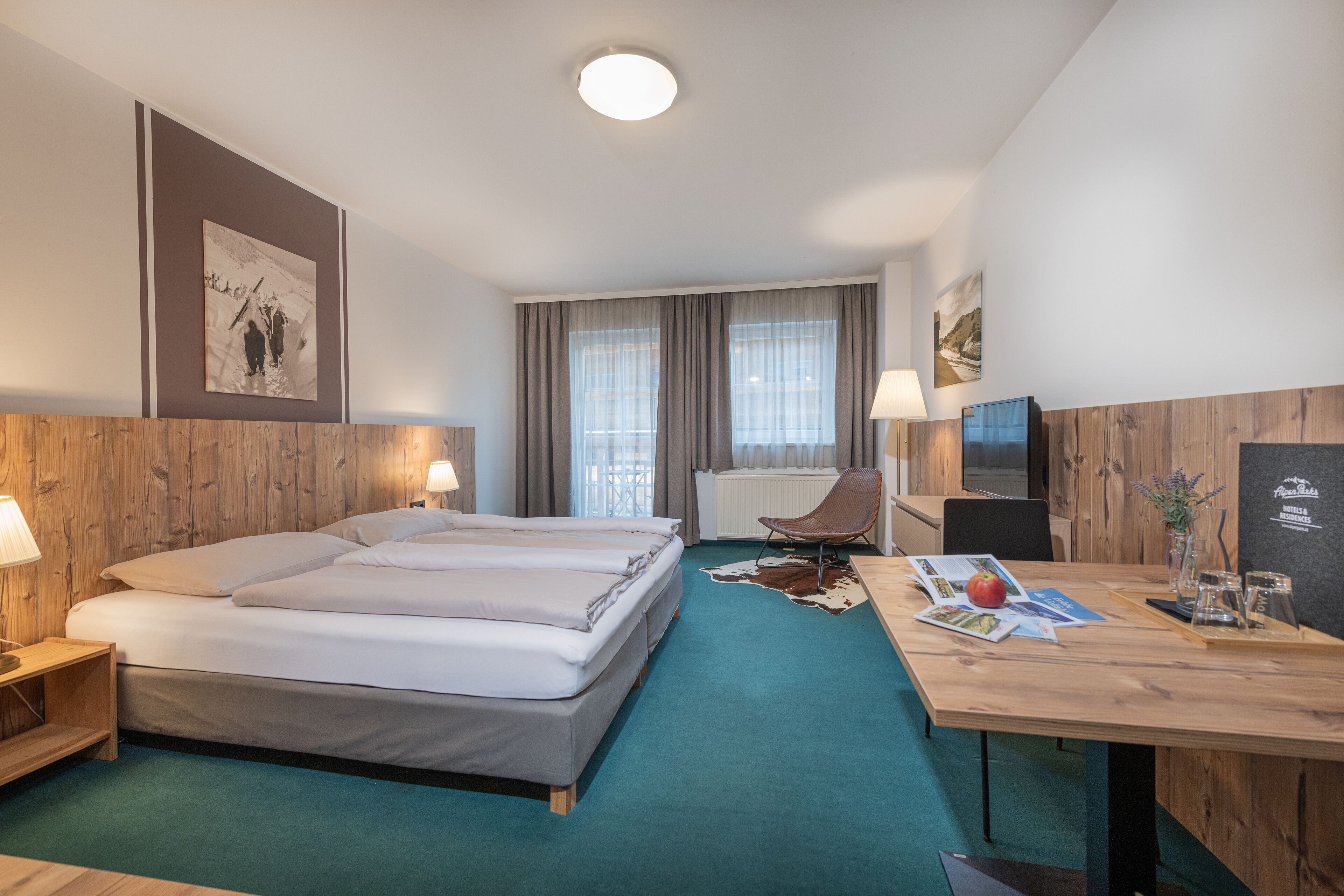 Een hotelkamer met een groot bed, een bureau met lamp, een stoel, een televisie en een raam met gordijnen.